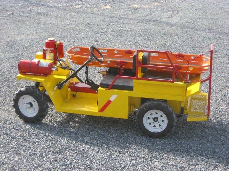 Yellow rescue vehicle with a stretcher, on gravel.