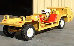 Yellow airport tug vehicle with a red seat and white wheels parked outside a building.