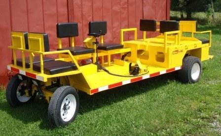 Yellow multi-passenger trailer with black seats on a grassy area.