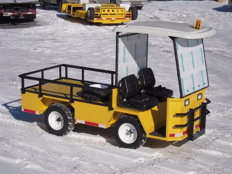 Yellow utility cart with two seats and a canopy on snowy ground.