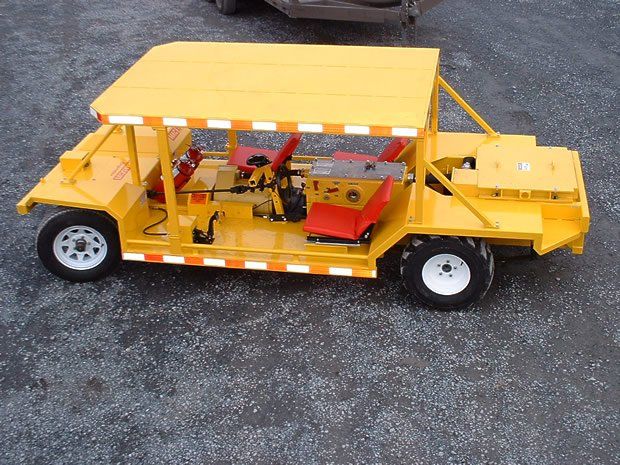 Yellow utility vehicle on gravel, with open sides and tools inside. Reflective tape on the sides.
