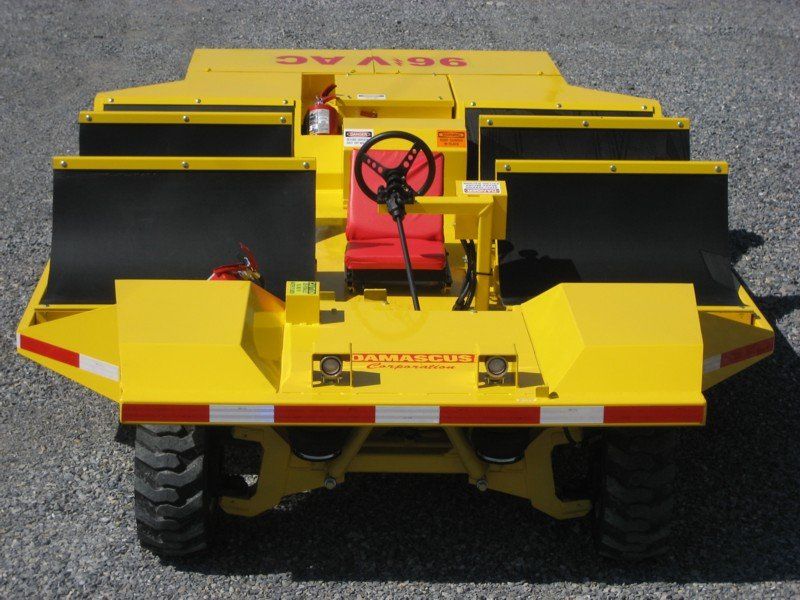 Yellow industrial vehicle with black screens, red seat, and black steering wheel, outdoors.