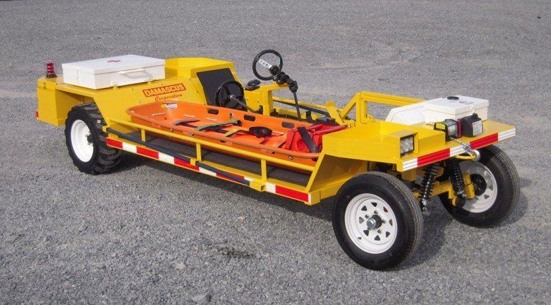 Yellow medical transport vehicle with gurney, medical supplies, and lights, on gravel.