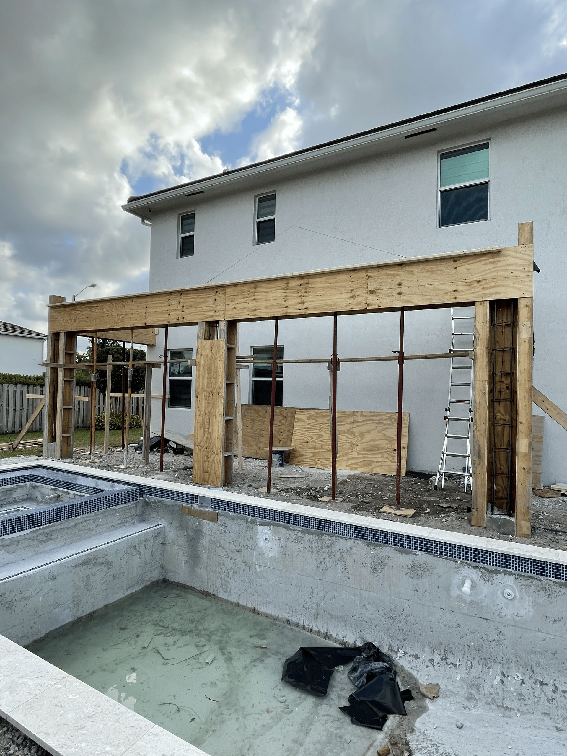 Construction of a patio cover next to a swimming pool and a two-story house.