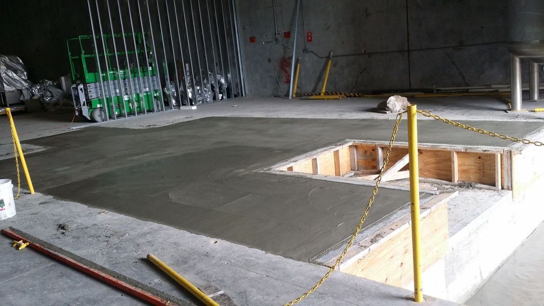 Concrete slab with an open pit, yellow safety poles, construction setting.