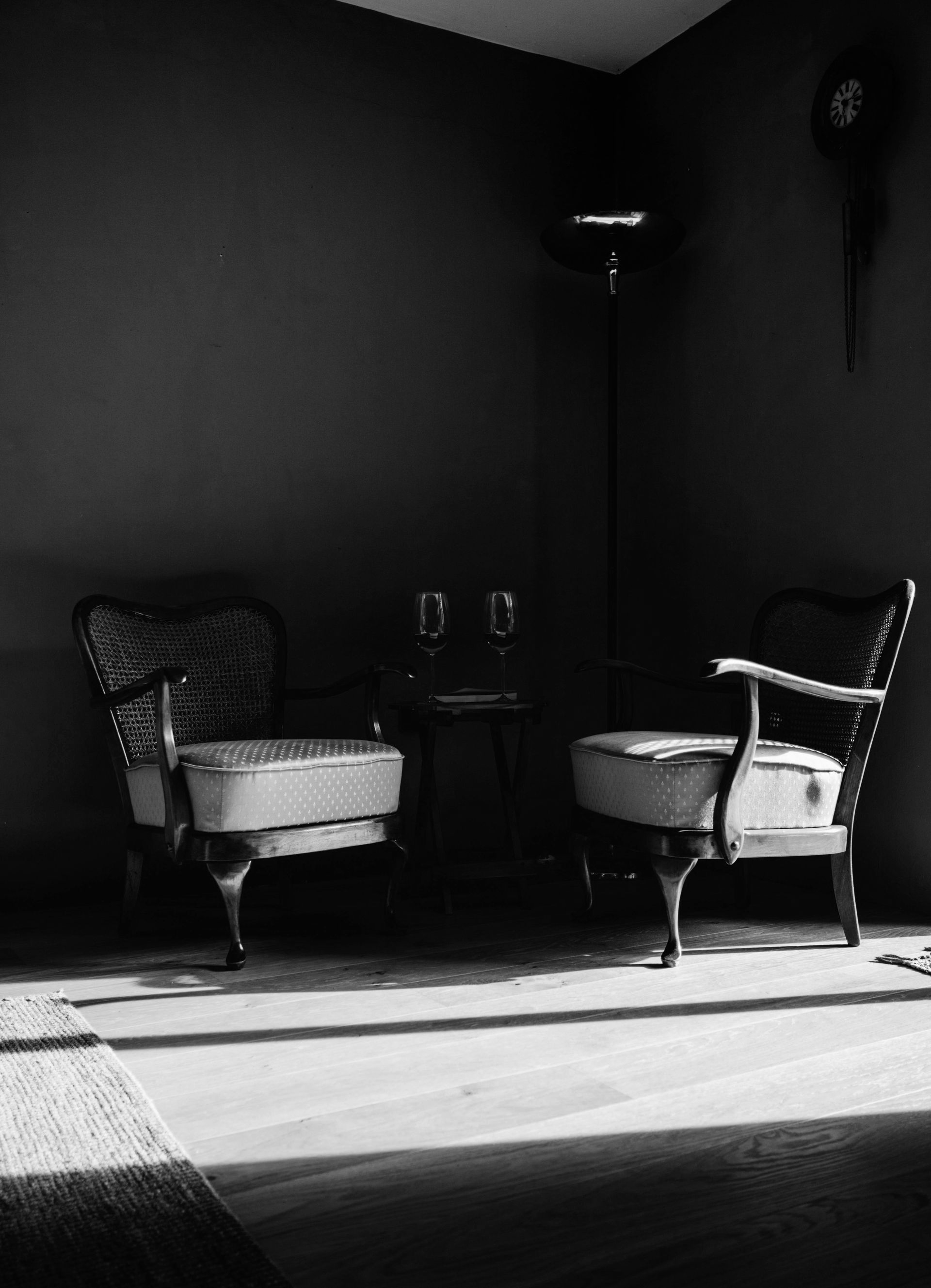 Two vintage chairs face each other, a small table with glasses between them, in a dim room.