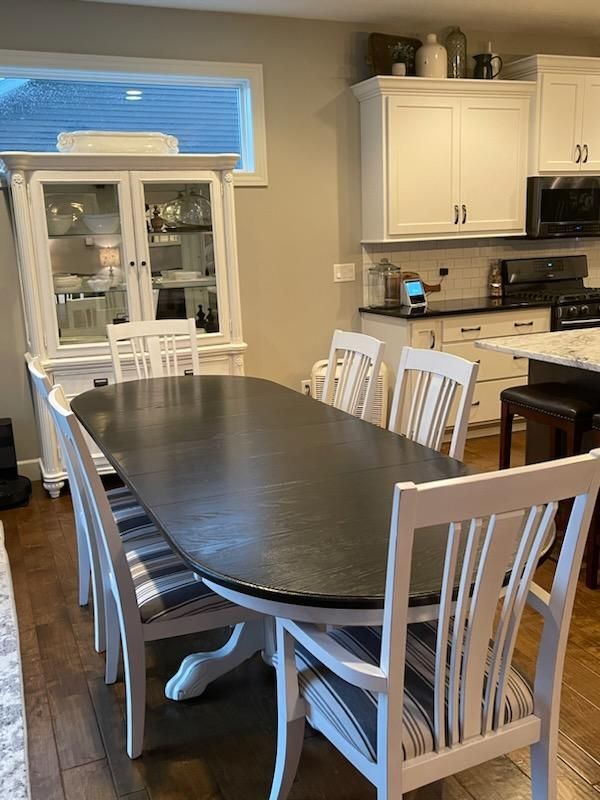 Dining room with a dark oval table, white chairs, and a white china cabinet in a bright kitchen.