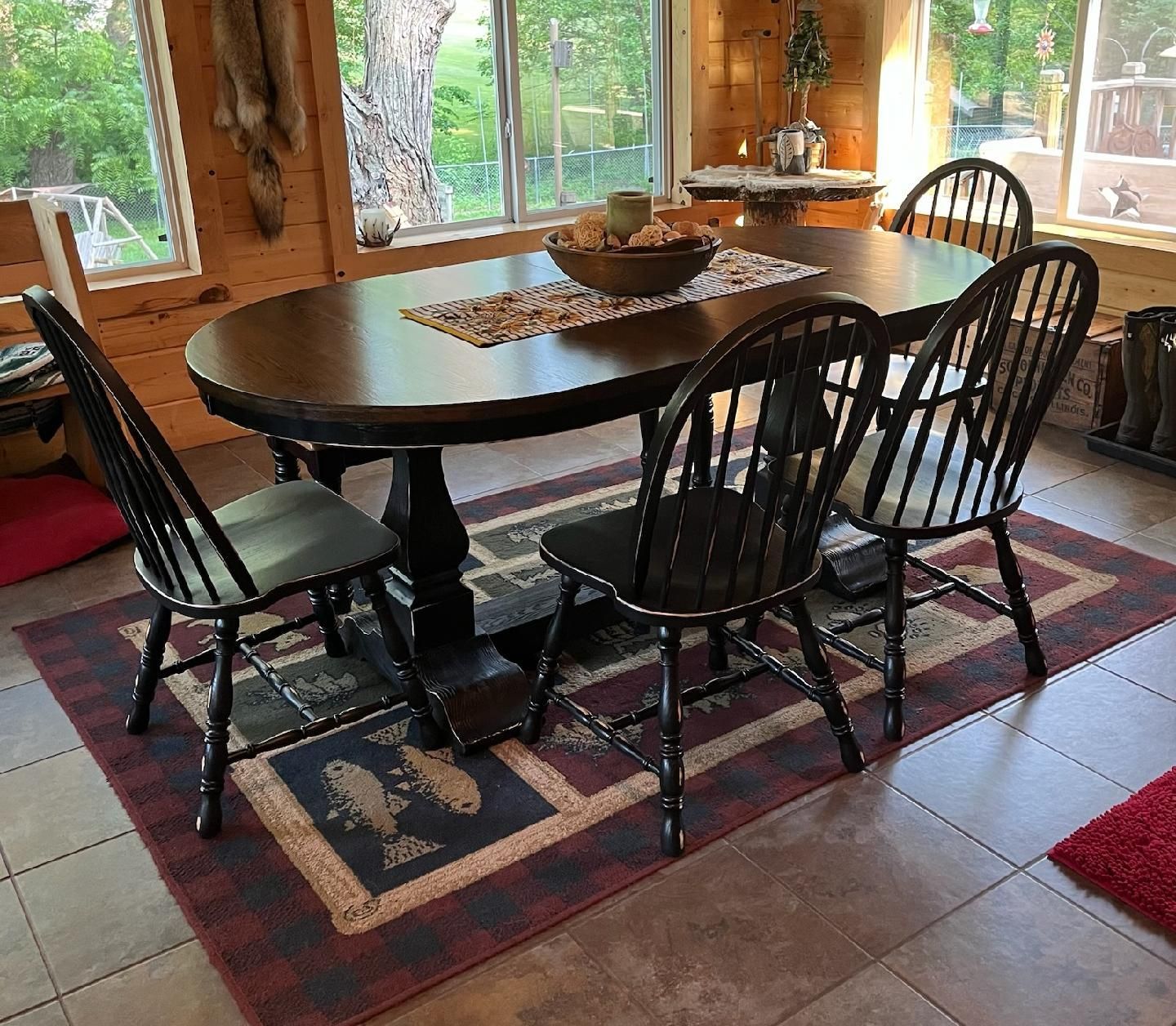 Dining table with black chairs on a red-and-blue rug in a sunlit room with large windows