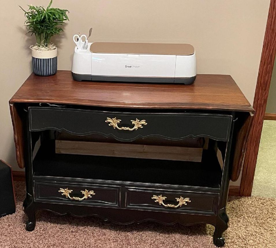 Dark wood cabinet with a white Cricut machine and a small potted plant on top.