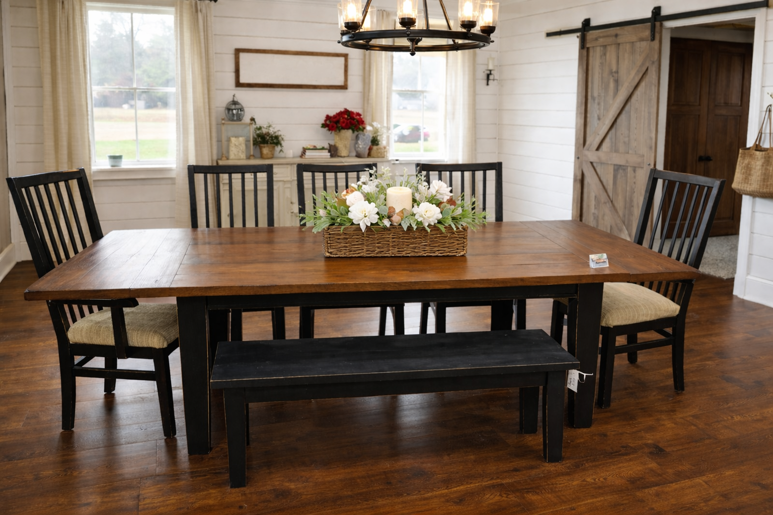 Dining room with a wooden table, black chairs, bench, and floral centerpiece in a rustic interior.