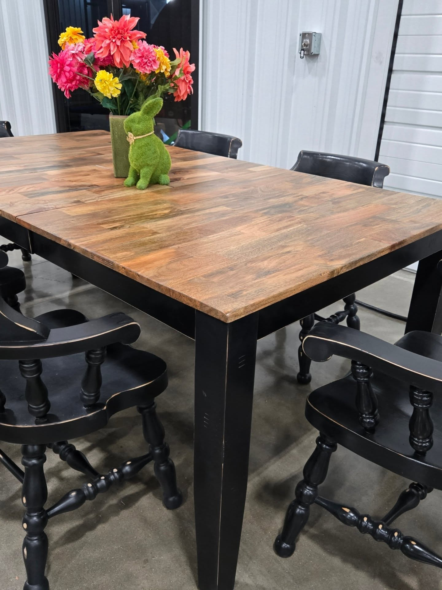 Wooden dining table with black chairs and a flower vase in a bright indoor room