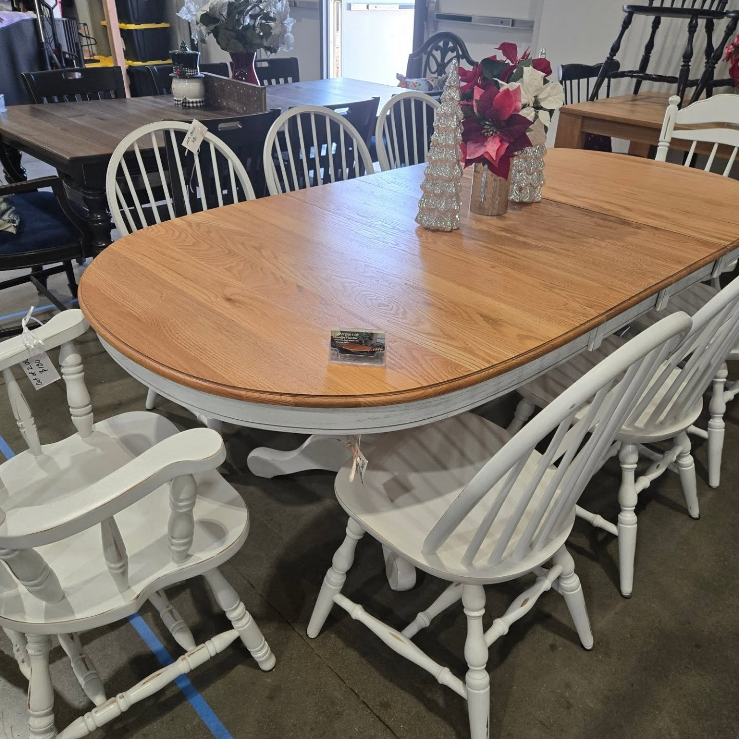 Large oval wooden dining table surrounded by white chairs in a furniture showroom