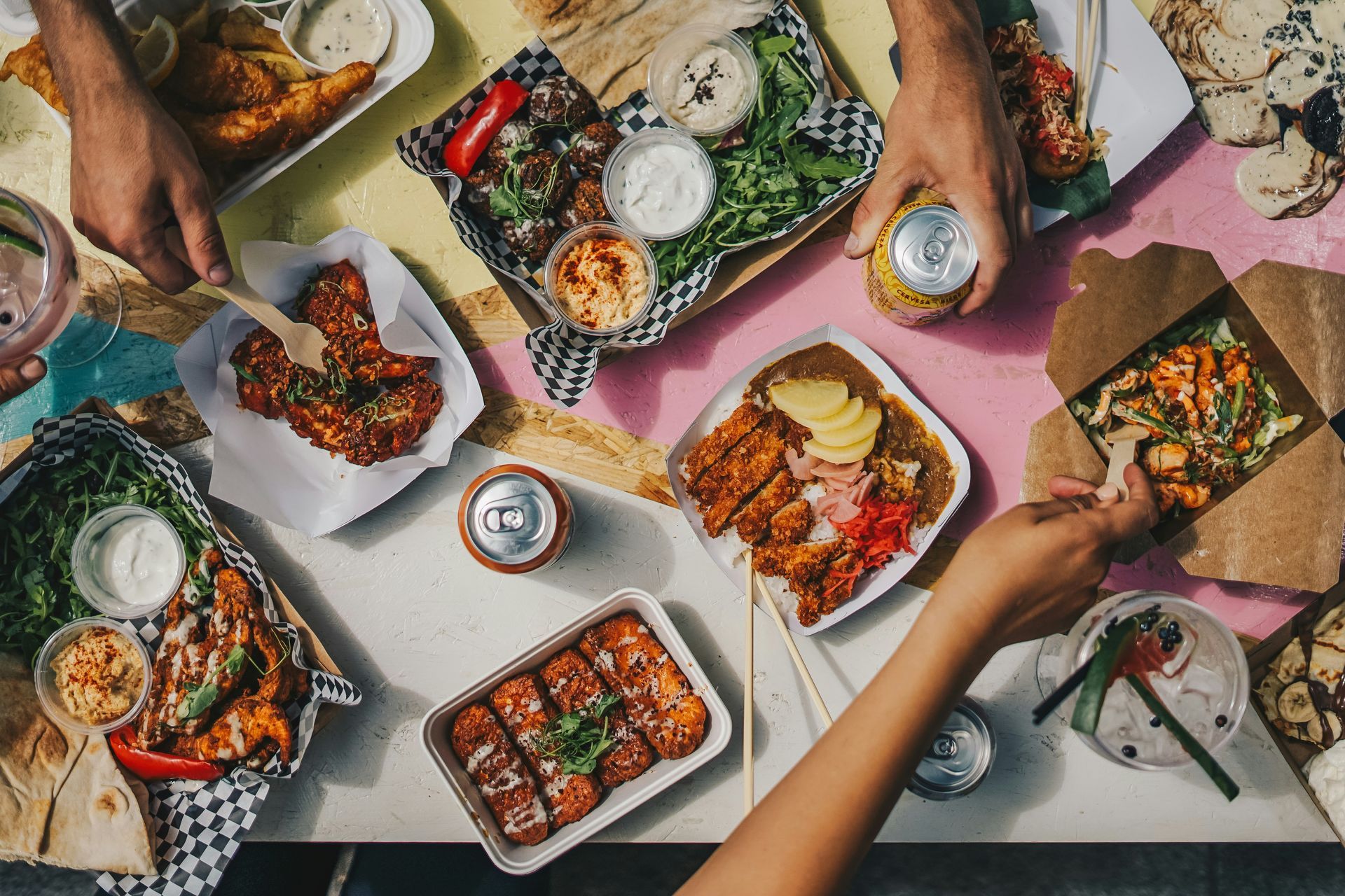 Three hands reach for a variety of takeaway meals on a table.