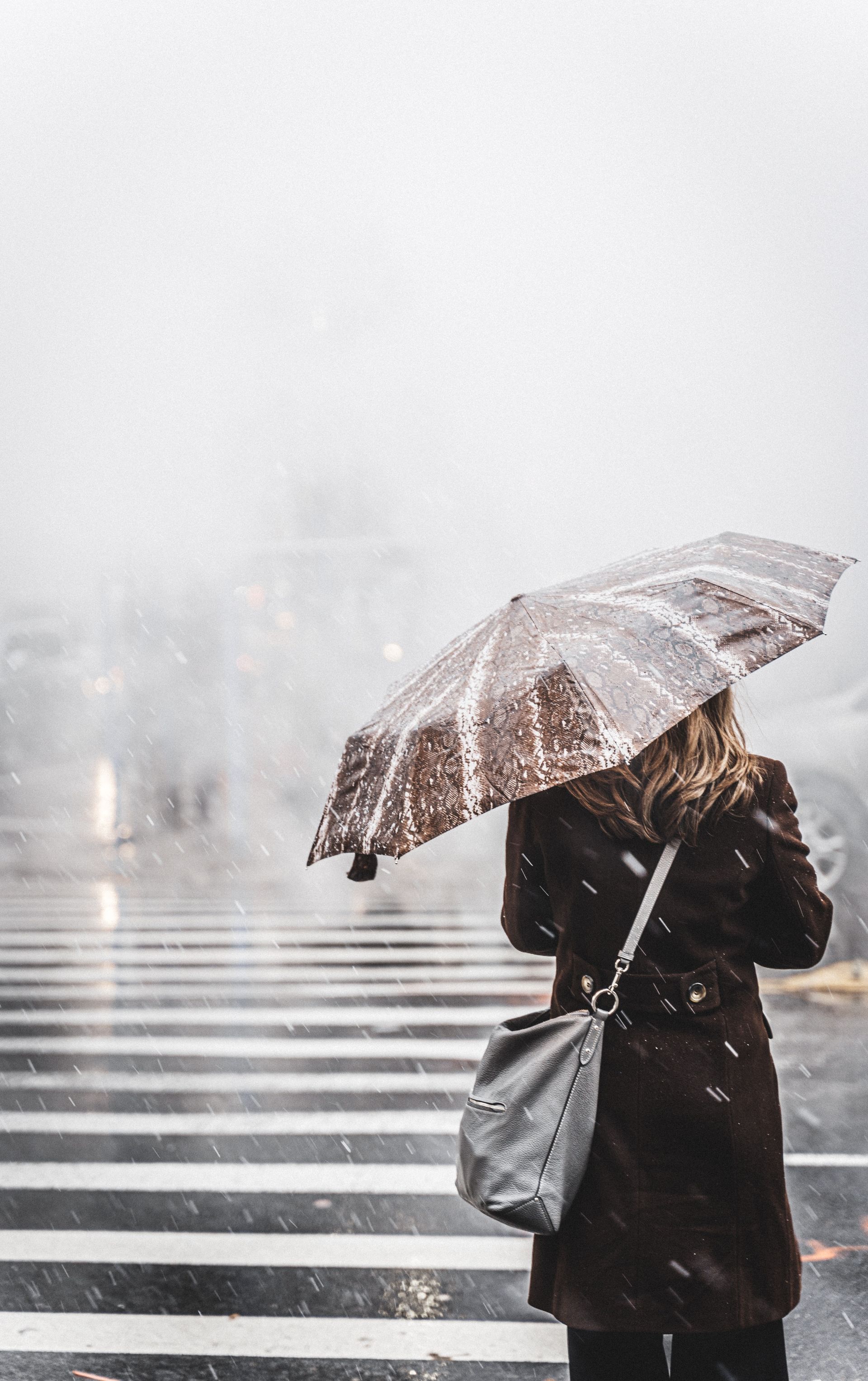 Woman with open umbrella, standing in the rain at a  crossing