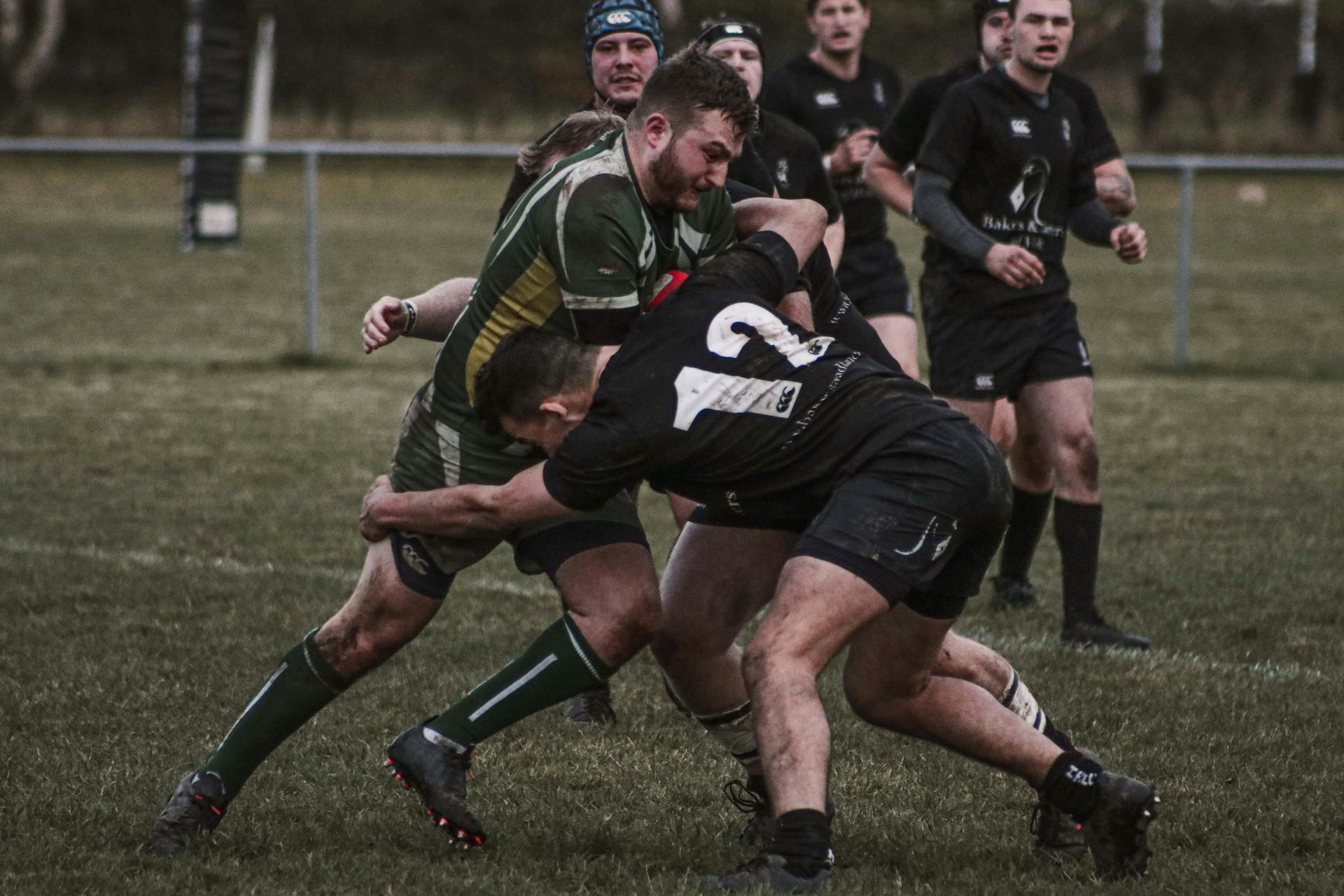 Rugby player carrying the ball while being tackled by two opponents.