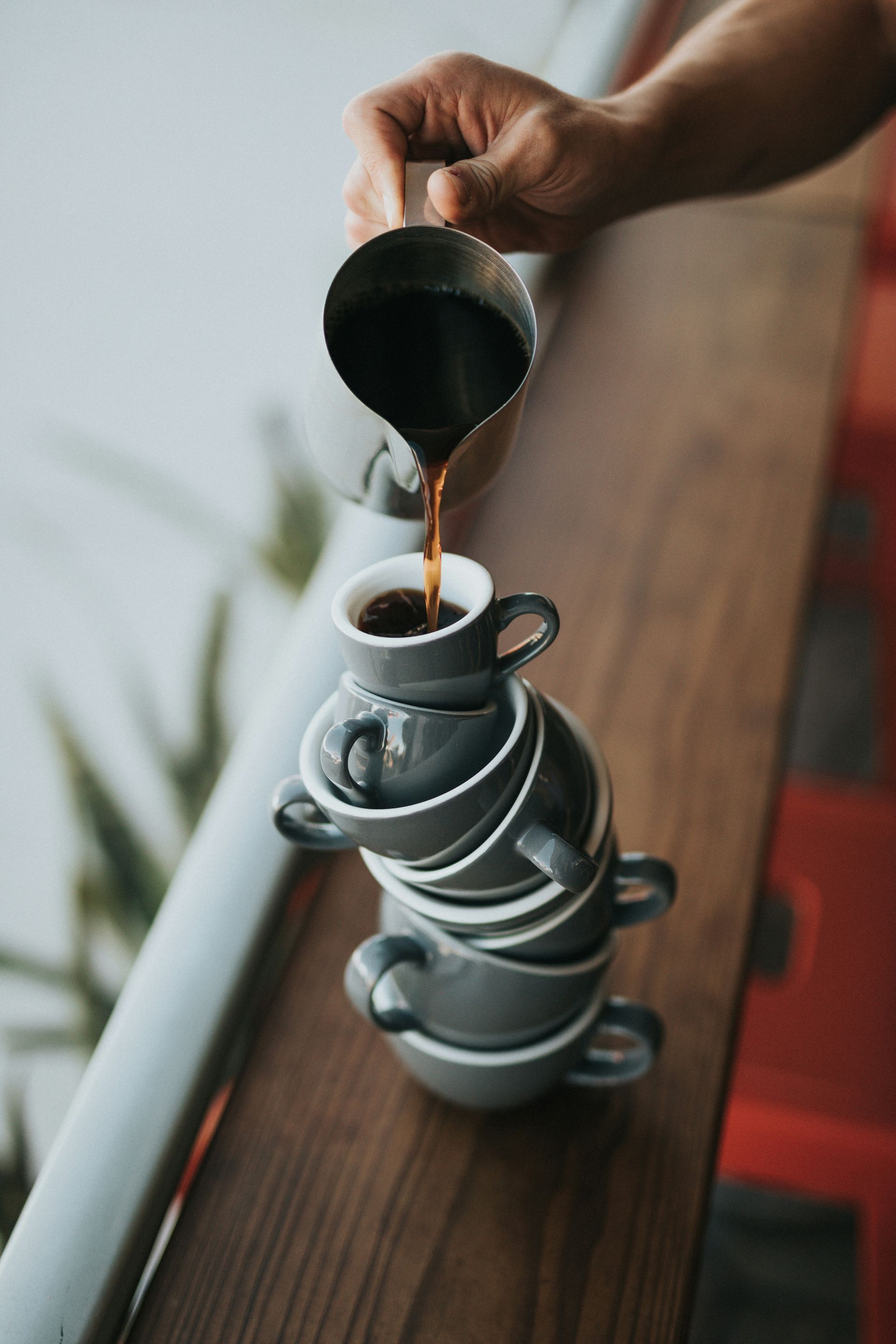 A person pouring coffee over a stack of cups.