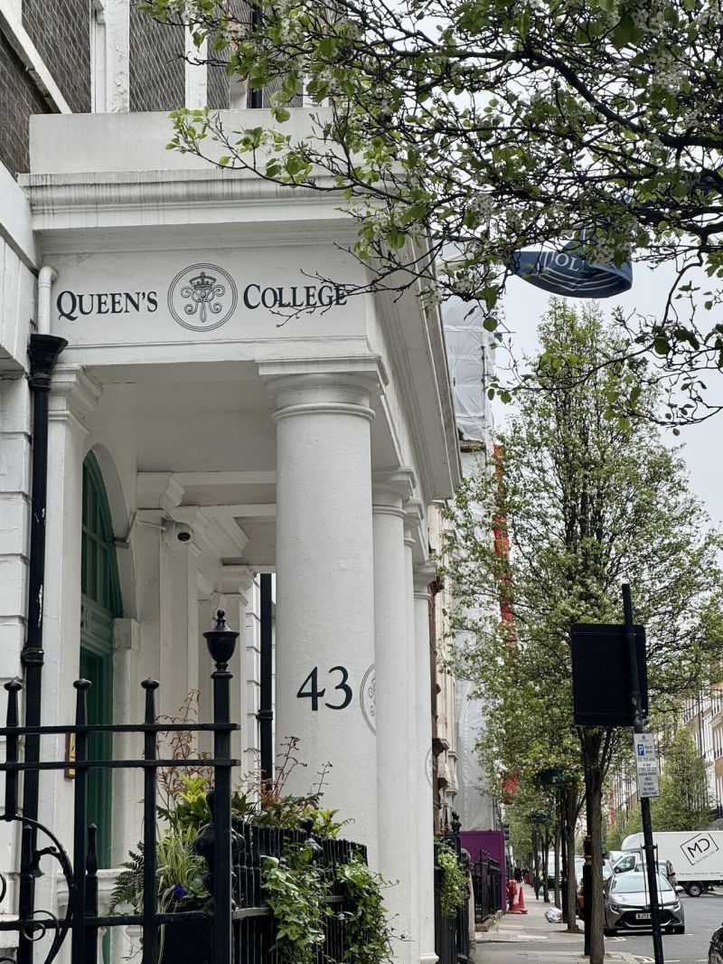 Street view of a white townhouse entrance with columns, iron gate, greenery, and the number 43.