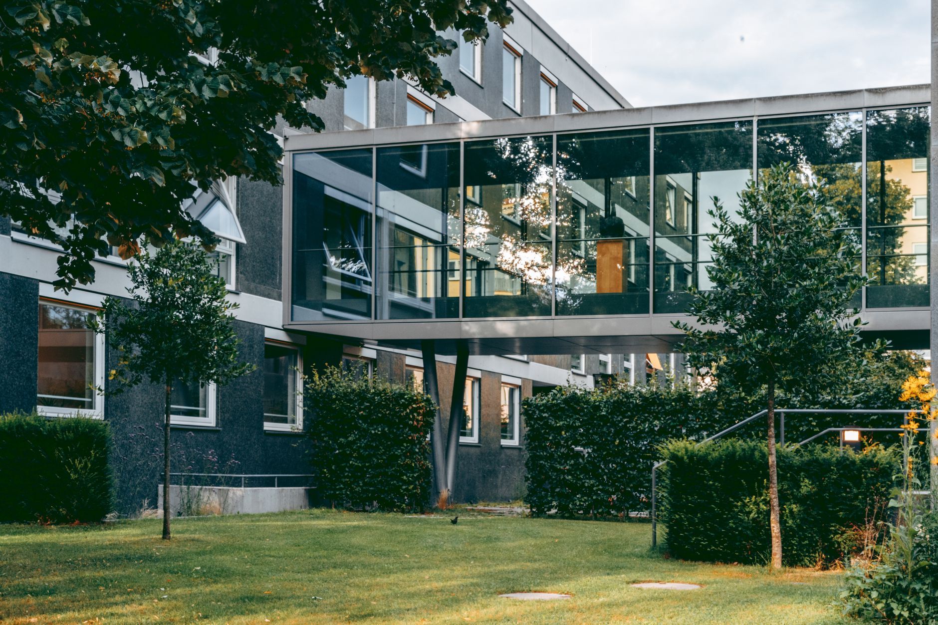 Modern building with a glass skybridge over a grassy courtyard and trees