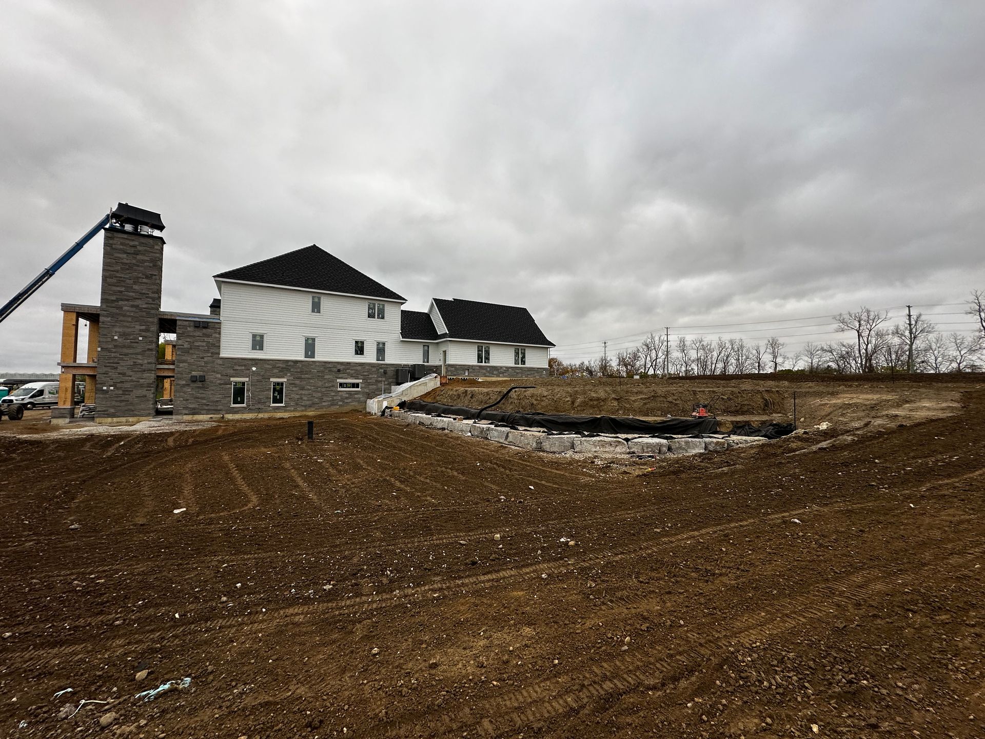 Large house under construction on a muddy site beneath a cloudy sky.