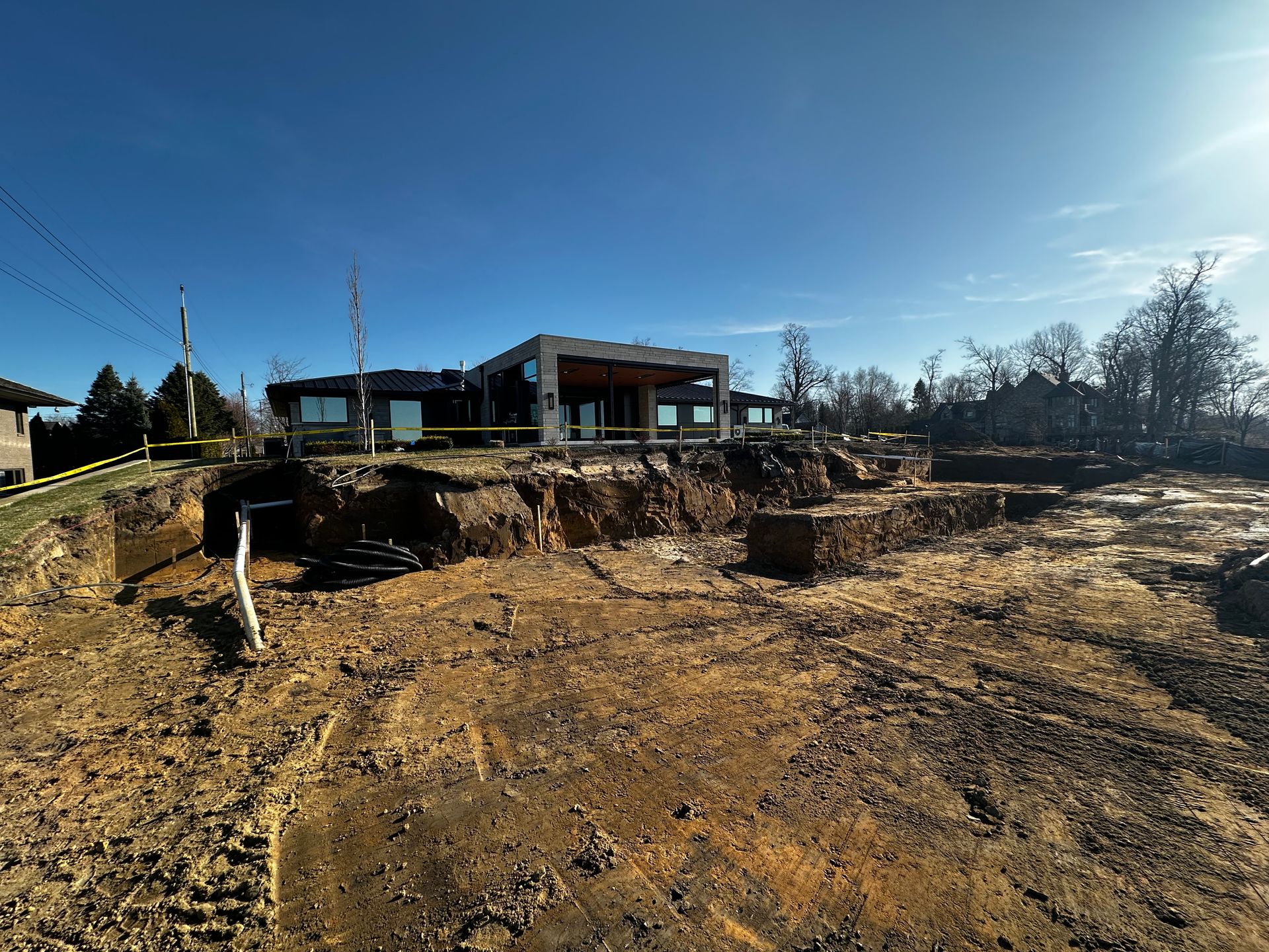 Wide dirt lot with a damaged ground area in front of a house under a clear blue sky