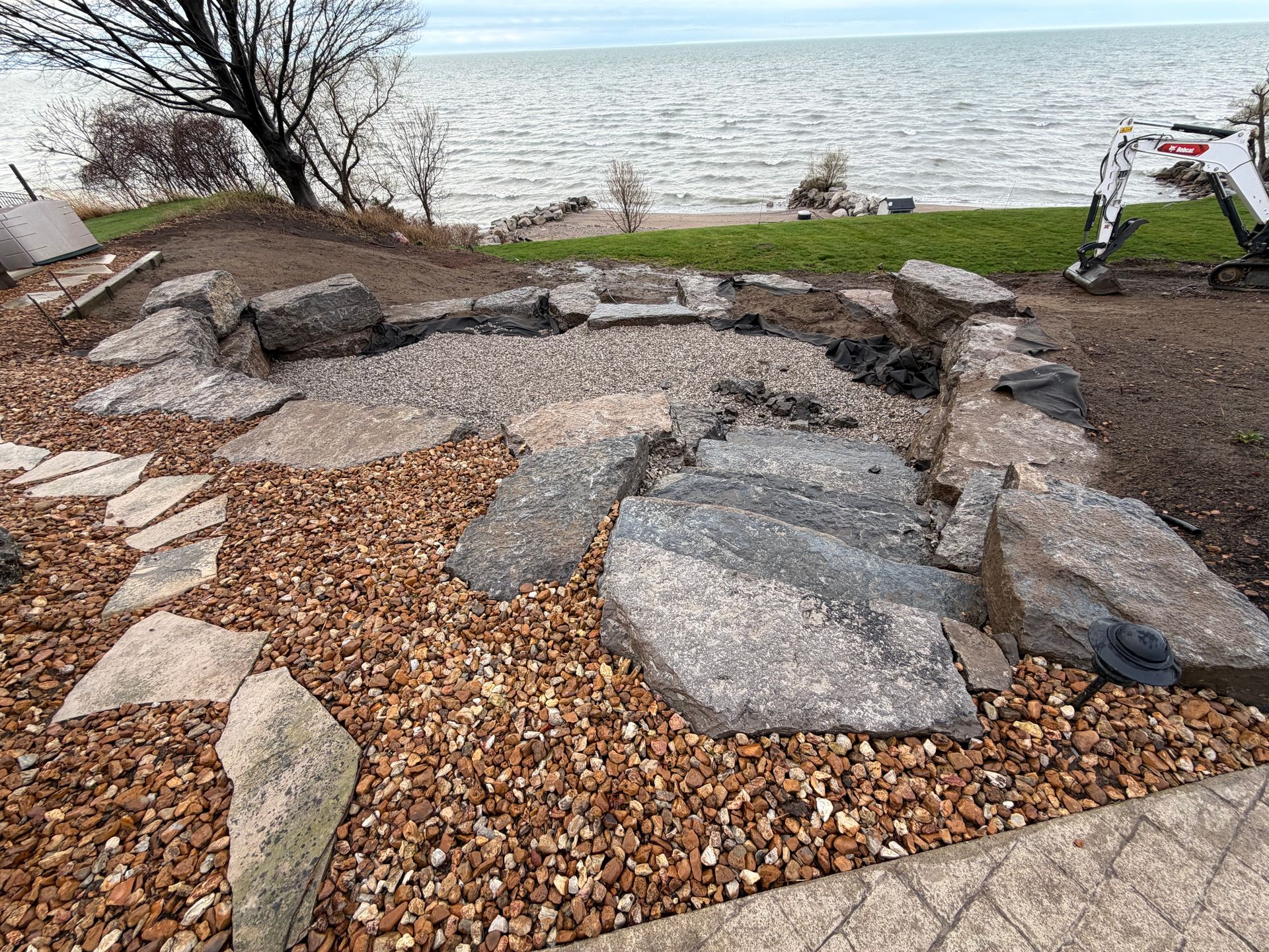Rock garden by a lakeshore with large stones, gravel, and an excavator nearby