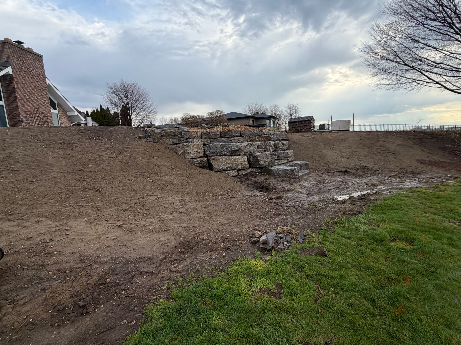 Mound of dirt and stacked stones beside a grassy strip under a cloudy sky