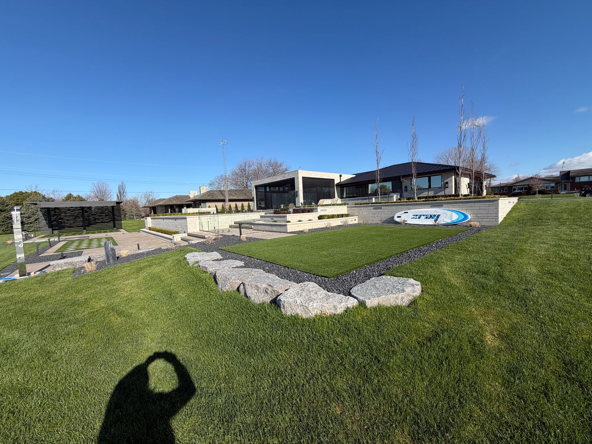 Grassy park with stone paths, benches, and modern buildings under a clear blue sky