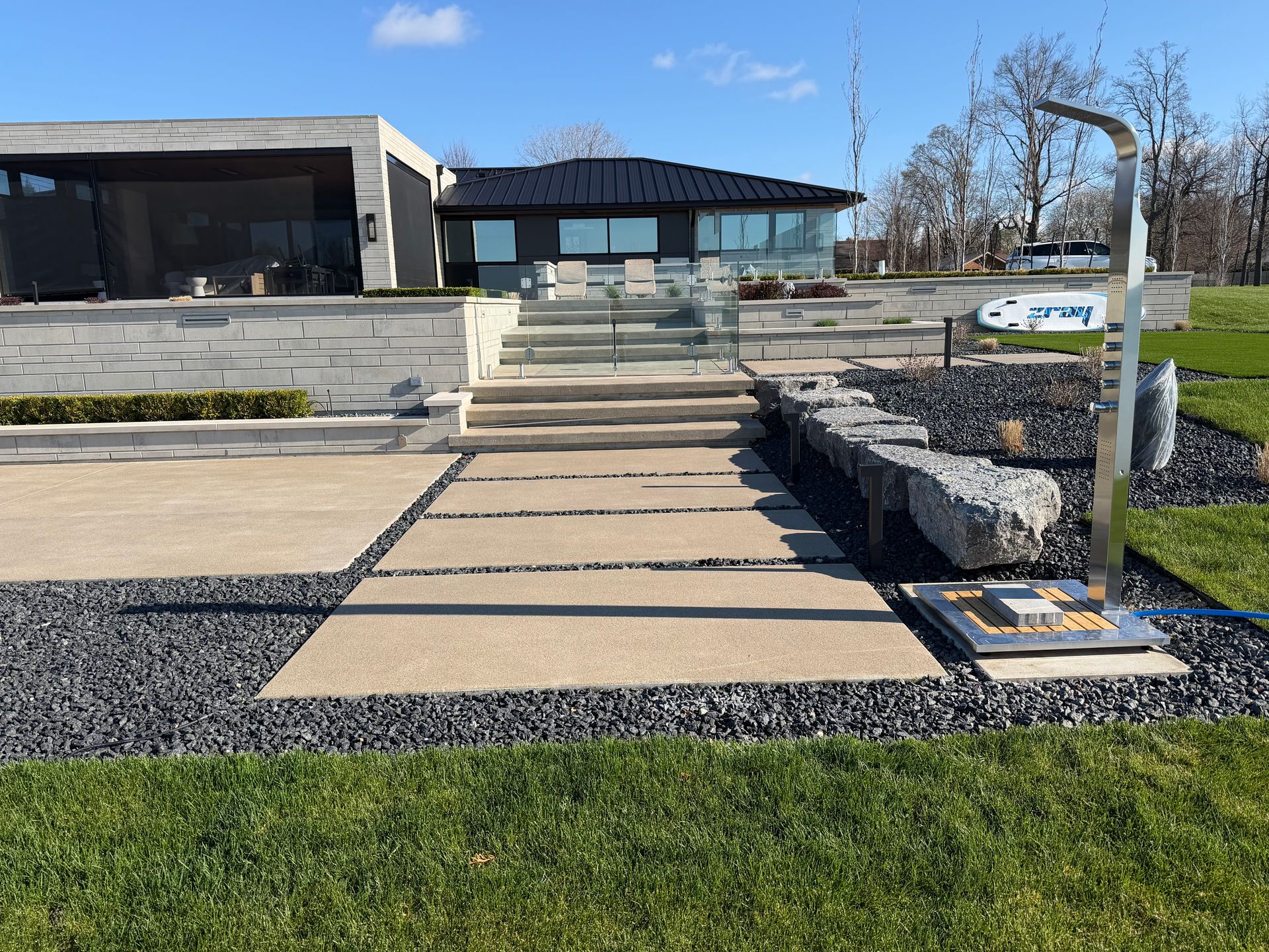 Modern building entrance with wide concrete steps, accessible ramp, and landscaped gravel walkway under a blue sky
