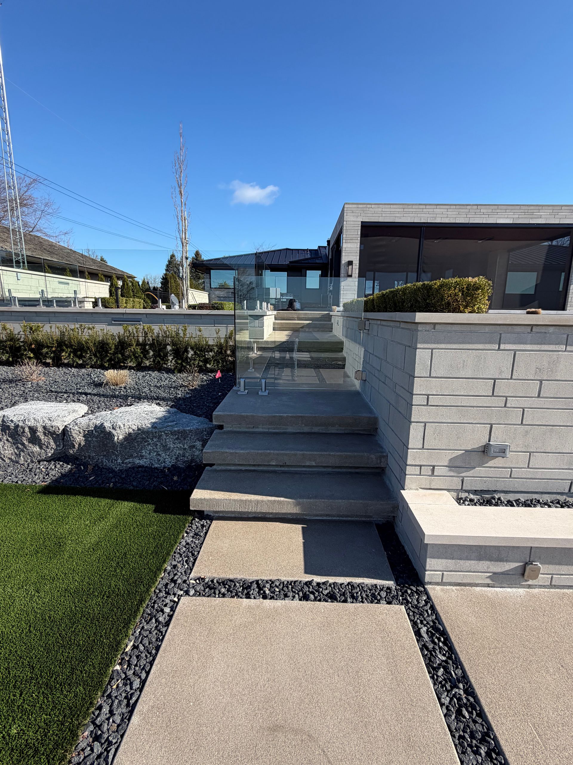 Modern house entrance with concrete steps, stone walls, and a blue sky.