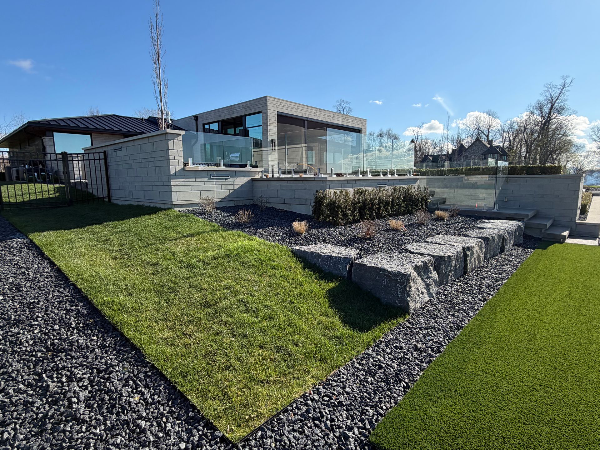 Modern house with glass walls, stone landscaping, and green lawn under a blue sky