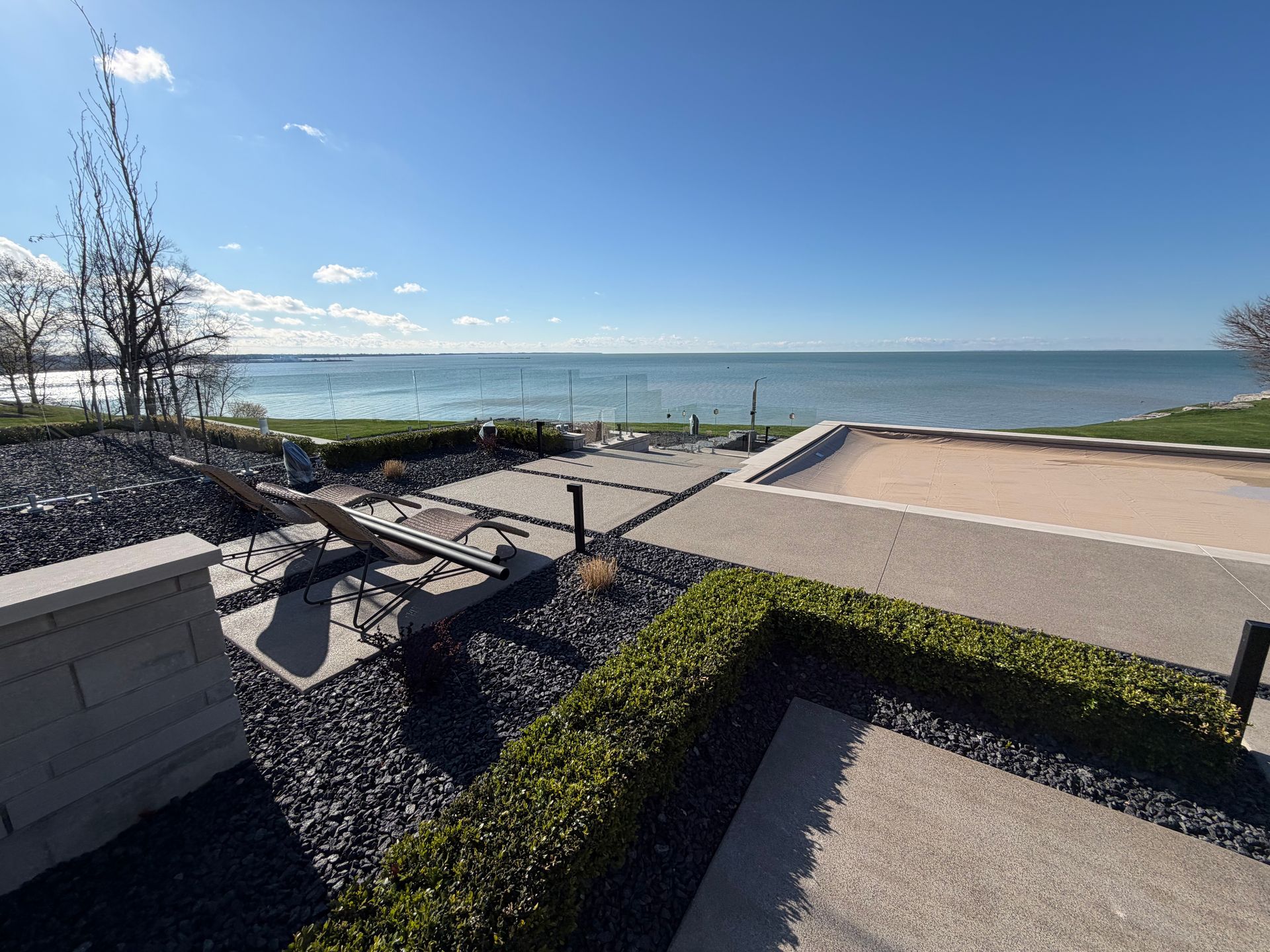 Modern seaside patio with stone benches, gravel landscaping, and a calm ocean horizon under a clear blue sky