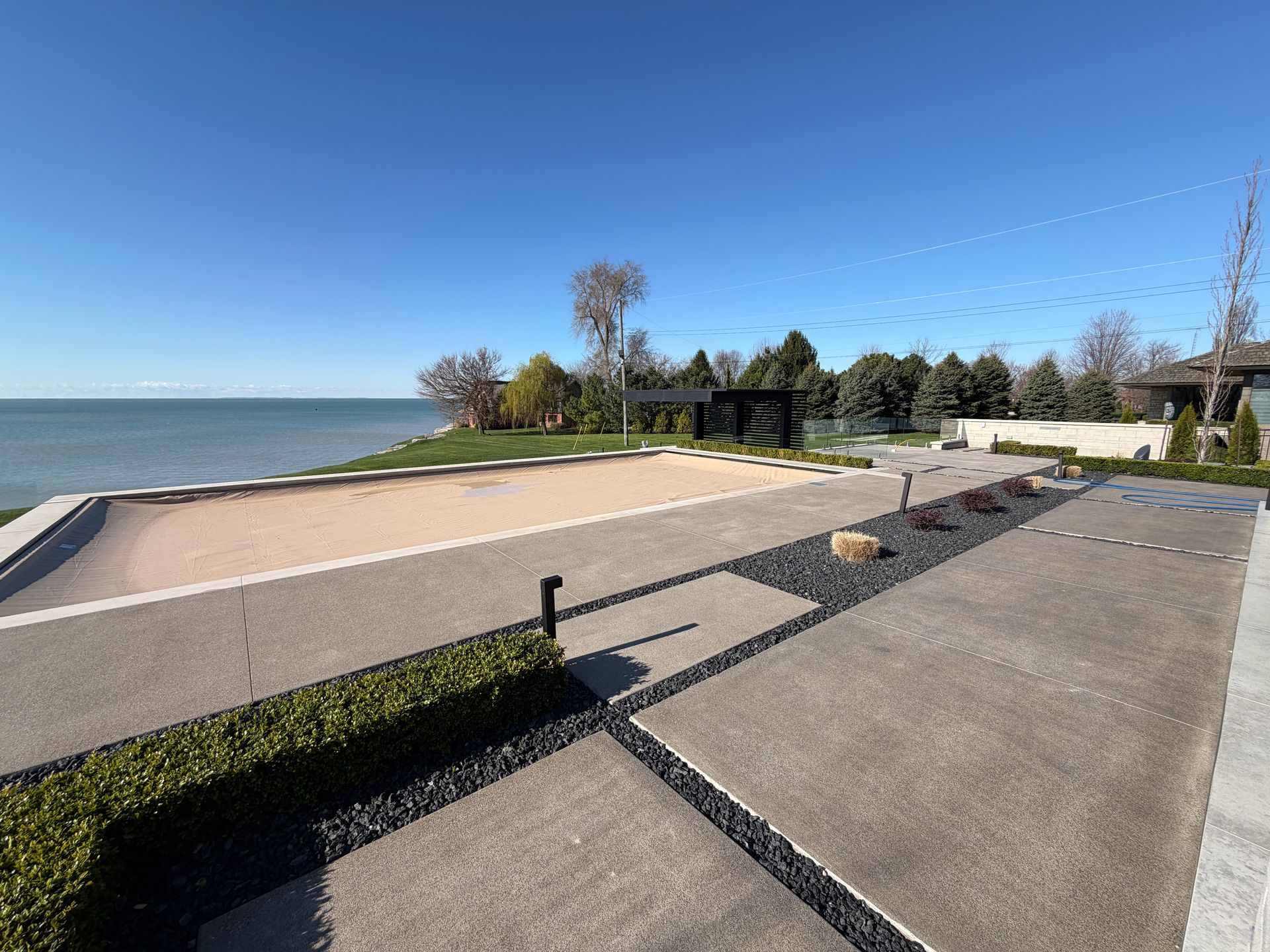 Lakefront walkway with concrete path, sandy beach, trees, and blue sky on a sunny day