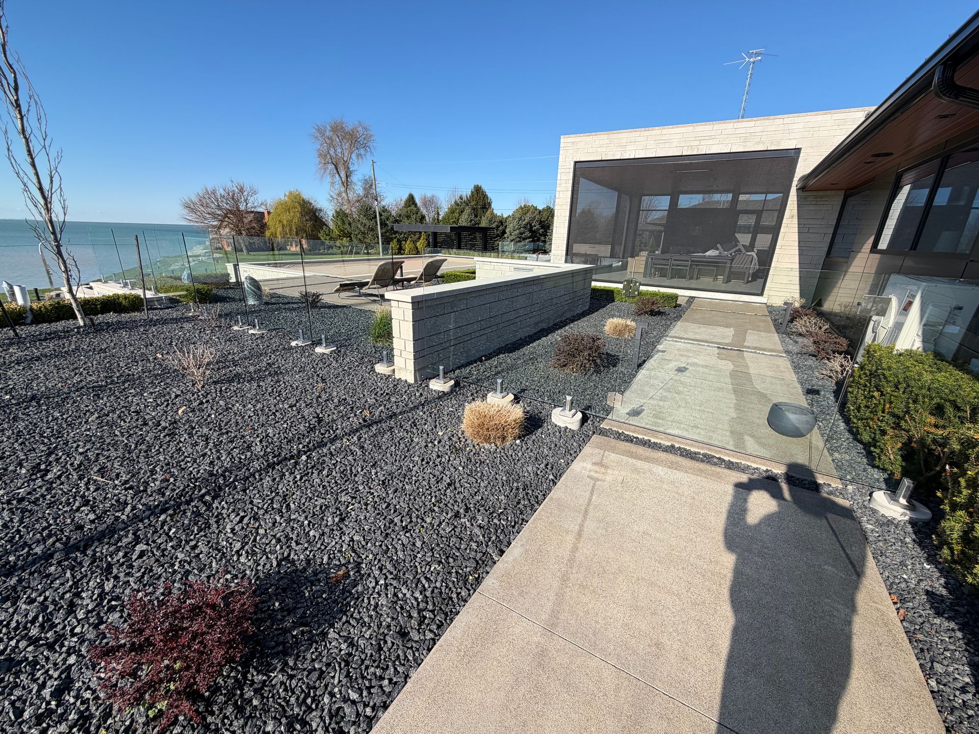 Modern landscaped courtyard with gravel beds, a concrete path, and a small building by the water.