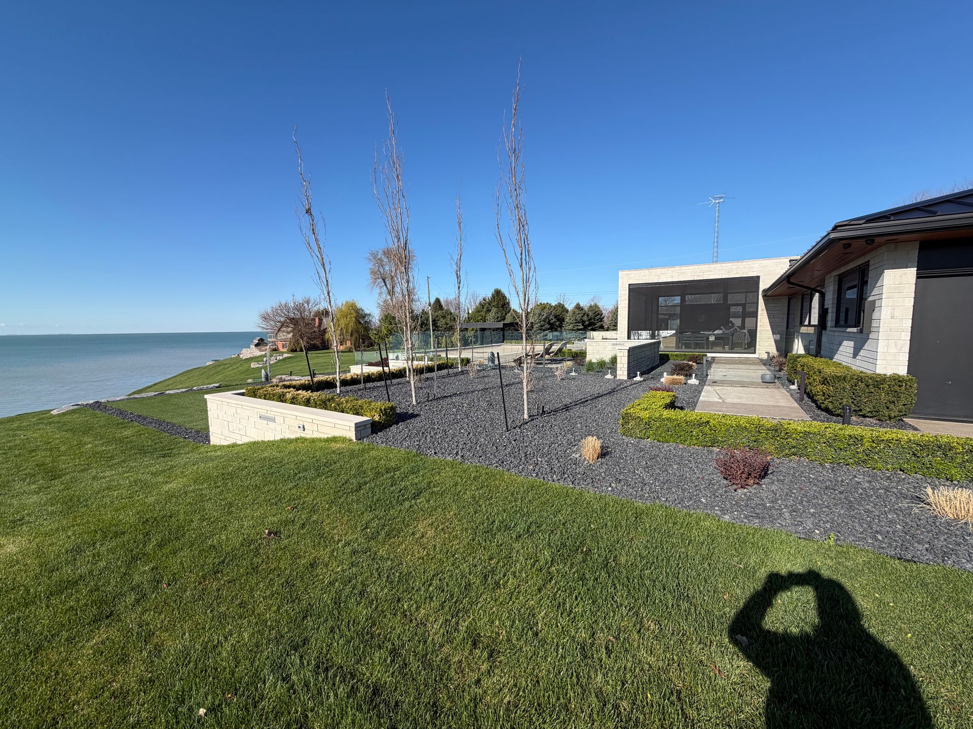 Lakeside modern house with landscaped rock garden, lawn, and blue sky