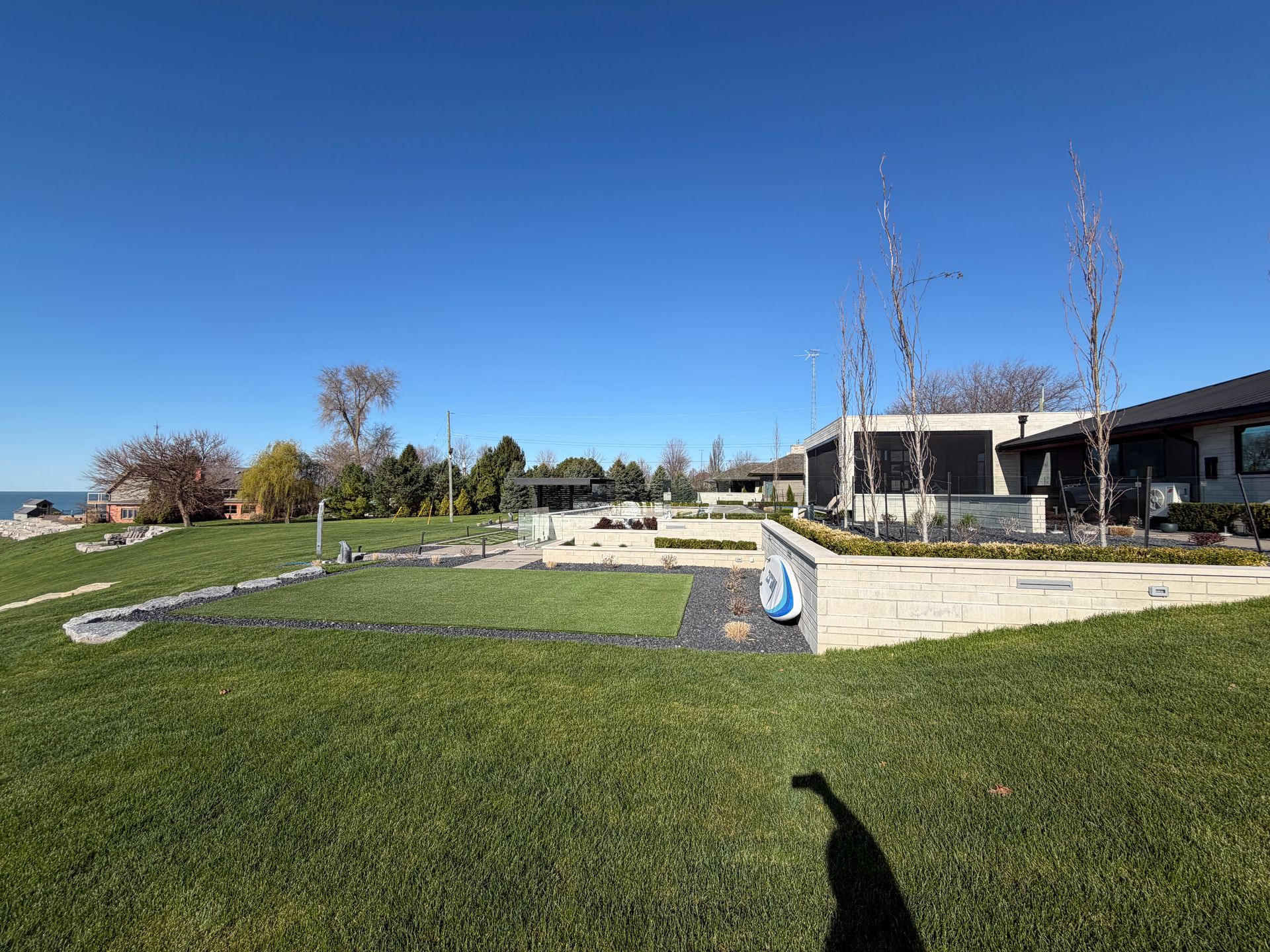 Modern outdoor patio and lawn under a clear blue sky, with stone seating and a water feature