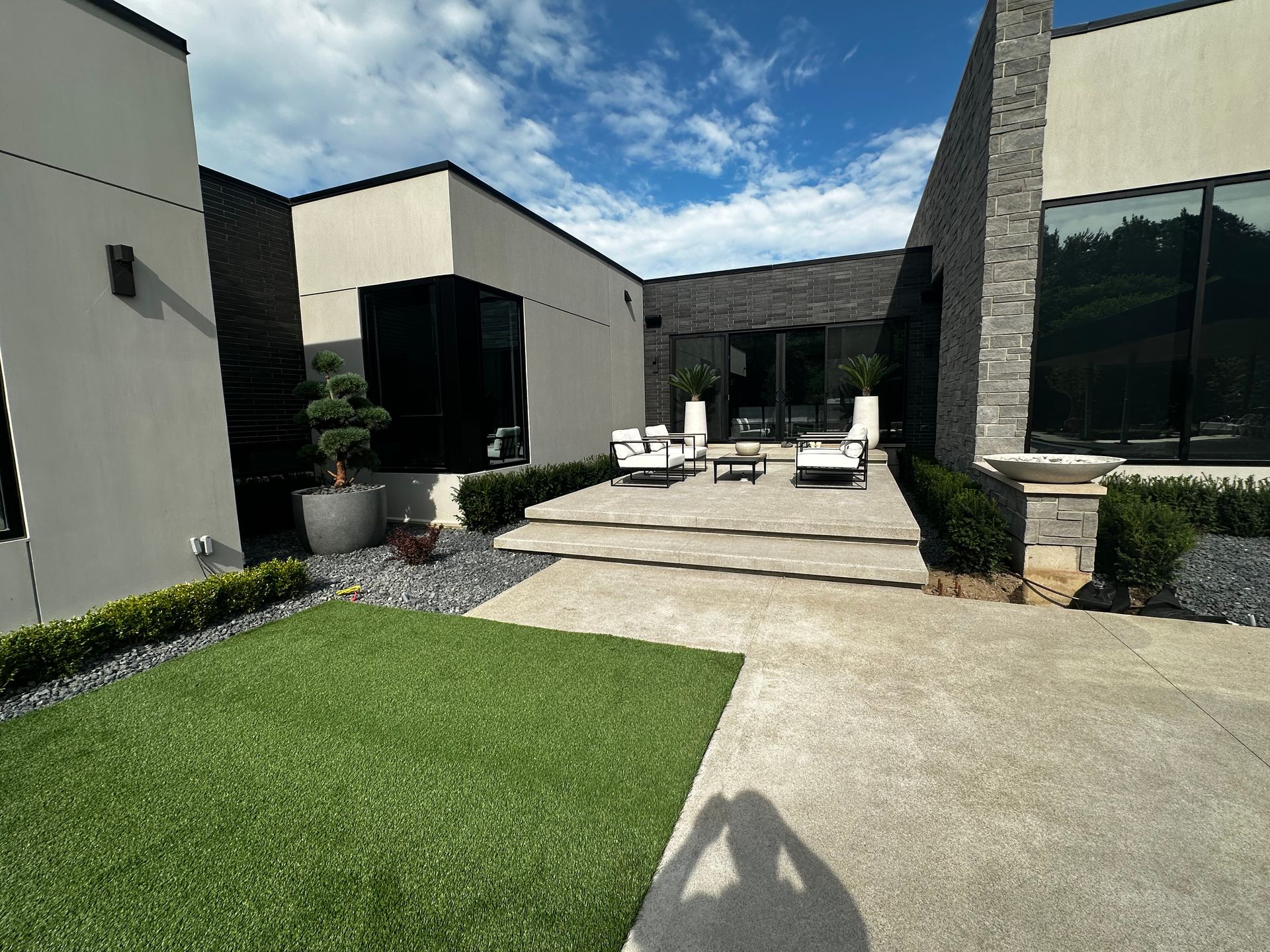 Modern courtyard with concrete path, green lawn, lounge chairs, and tall windows under a blue sky
