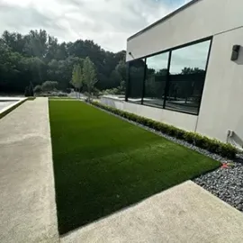 Modern building exterior with large windows, green lawn, concrete path, and landscaping stones