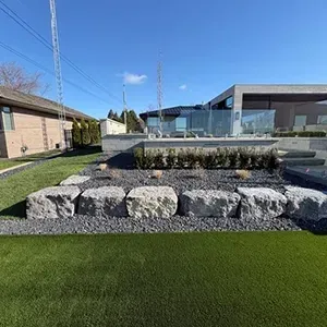 Landscaped plaza with stone planter, grass lawn, and low modern buildings under a blue sky