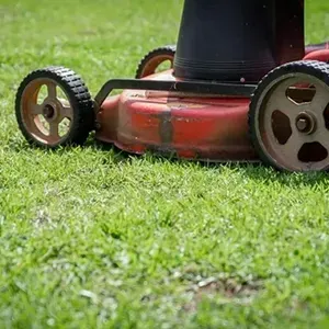 Red lawn mower on green grass, close-up of front wheels and cutting deck.