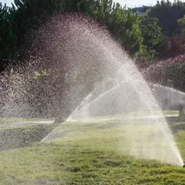 Lawn sprinkler spraying arcs of water across a sunny grassy park.