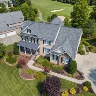Aerial view of a large suburban brick house with a gray roof, landscaped yard, and driveway