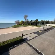 Concrete lakeside walkway with a sandy beach, calm water, and a blue sky