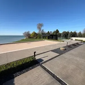 Concrete lakeside walkway with a sandy beach, calm water, and a blue sky