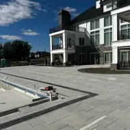 Modern apartment courtyard with tiled patio, shallow pool, and balconies under a blue sky