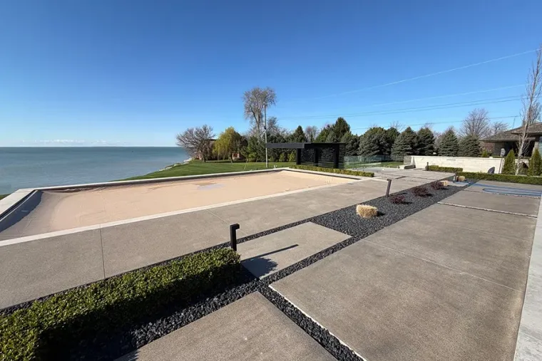 Concrete lakeside walkway with a sandy beach, calm water, and a blue sky