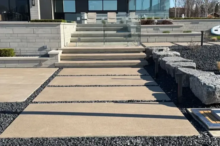 Stone walkway with wide steps leading to a modern building entrance, bordered by gravel landscaping.