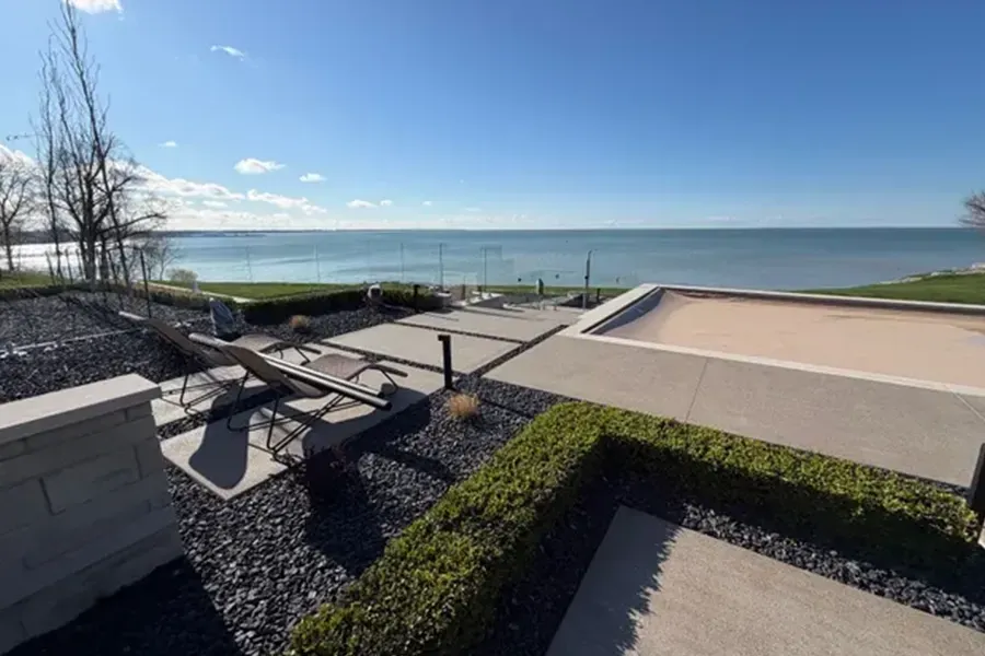 Modern waterfront terrace with benches, gravel planters, and a clear blue sky over calm water
