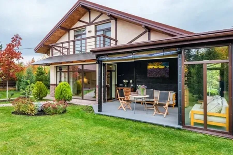 Modern house with a glass patio enclosure and outdoor seating on a green lawn