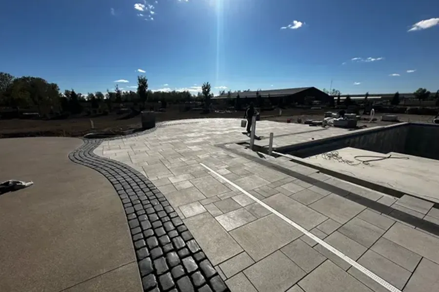 Bright sunny plaza with curved cobblestone path, stone steps, and a few people in the distance
