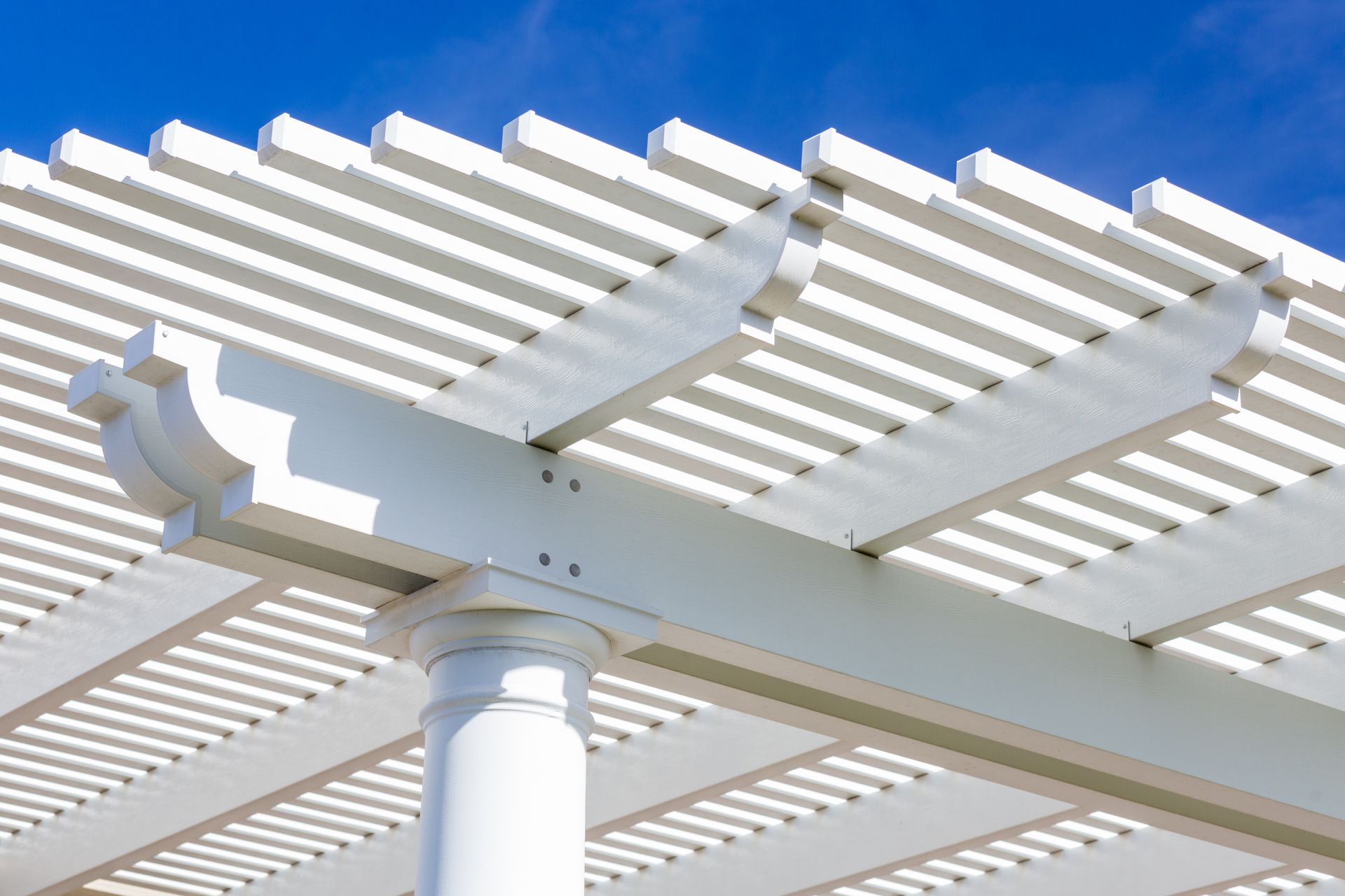 White pergola with horizontal beams, set against a bright blue sky.
